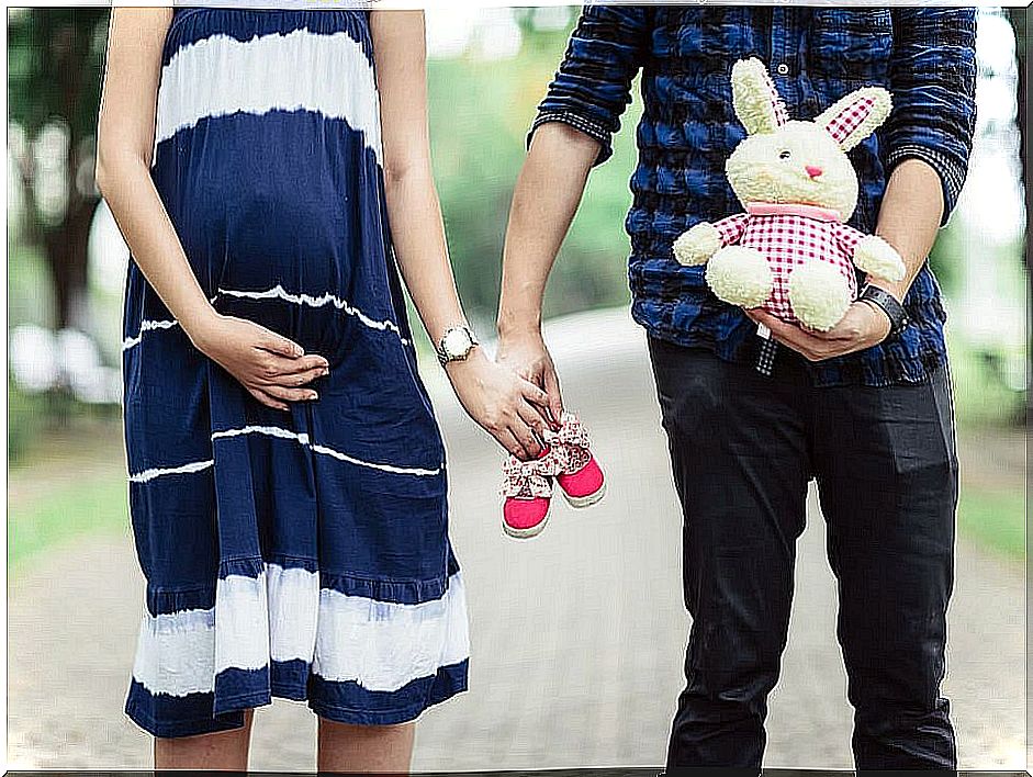 Pregnant couple with a teddy bear and baby shoes.