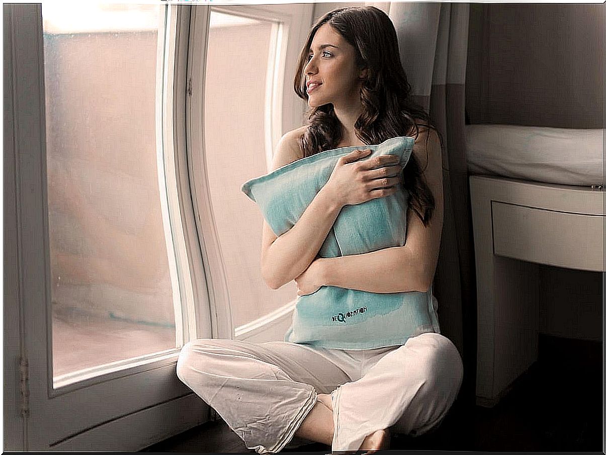 Woman hugging a pillow looking out the window.