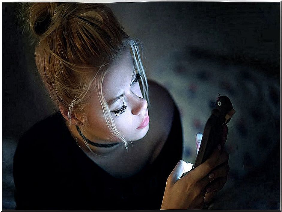 Young woman looking at her mobile phone in the dark.